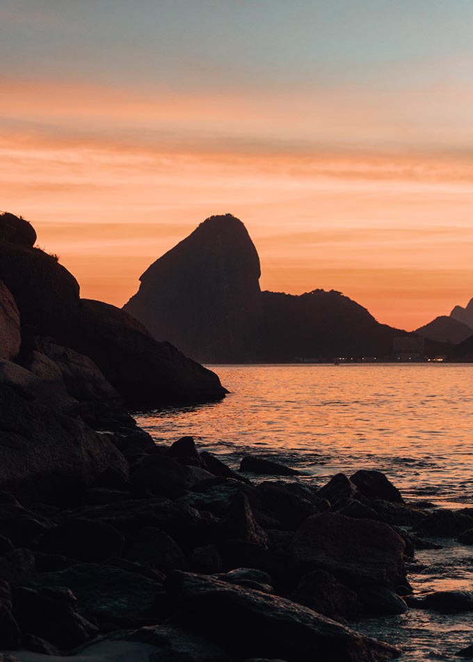 A vertical shot of beautiful rock formations near the sea with the sunset in the background in Rio de Janeiro